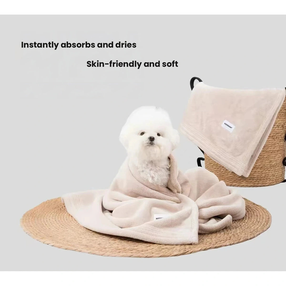 Small white dog wrapped in a beige HiDREAM pet bath towel beside a hanging towel